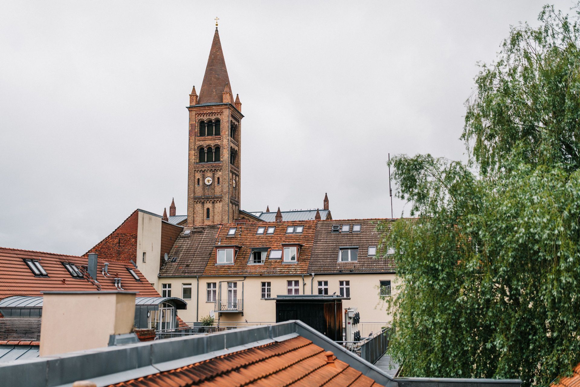Blick auf Wohnhäuser mit roten Dächern, im Hintergrund ein hoher Kirchturm.