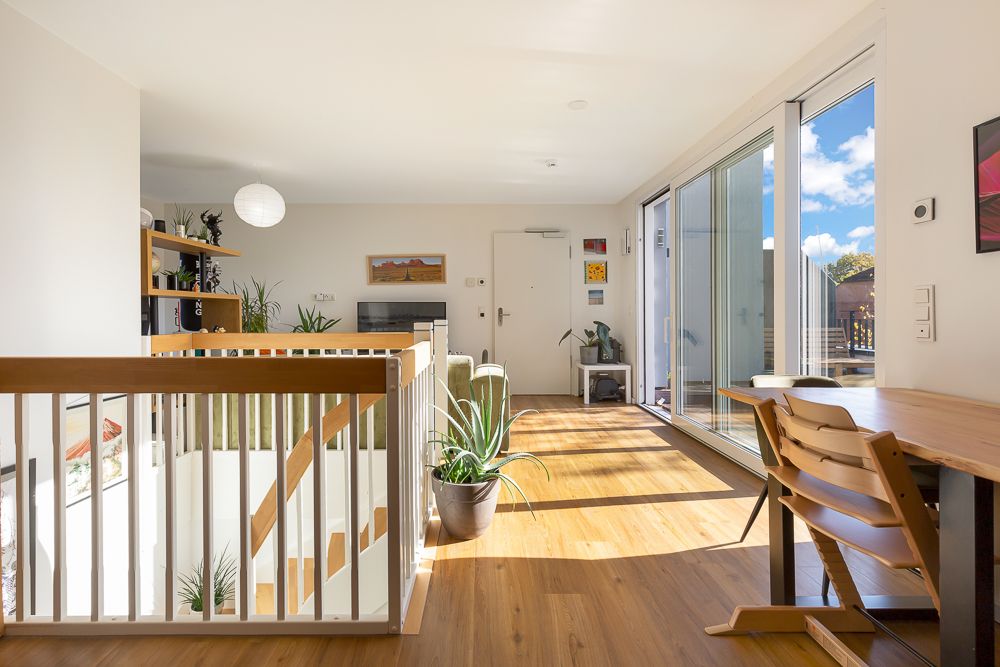 Helles Wohnzimmer mit Holzboden, Schreibtisch, Pflanzen und Zugang zu einem Balkon.