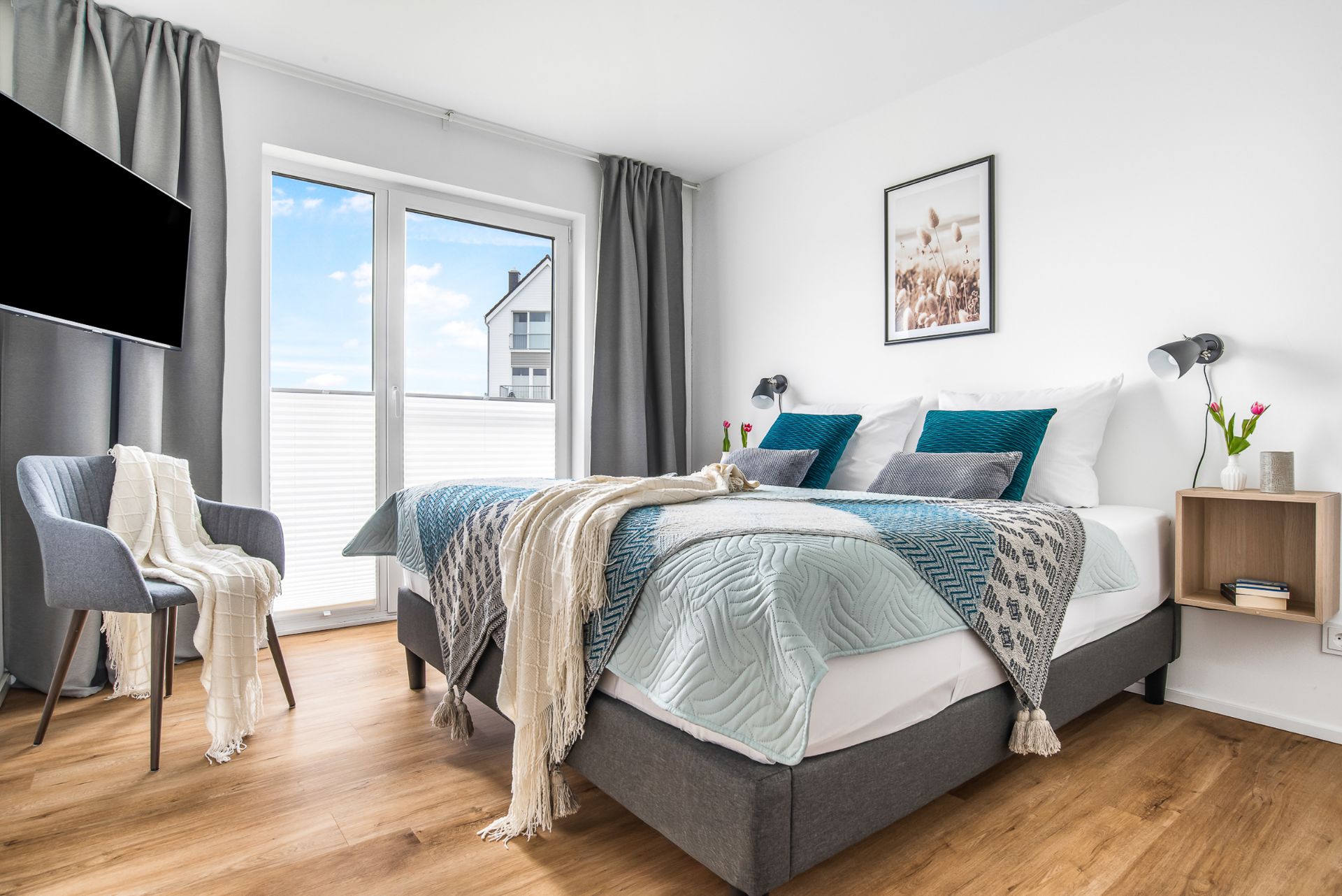Modernes Schlafzimmer mit Doppelbett, Fenster, grauen Vorhängen, Sessel und Holzboden.