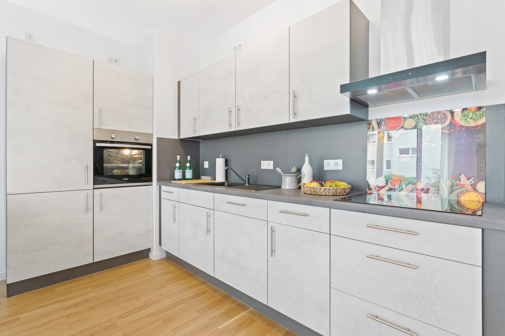 Moderne, helle Einbauküche mit grauen Schränken, Backofen und Obstkorb auf der Arbeitsplatte.