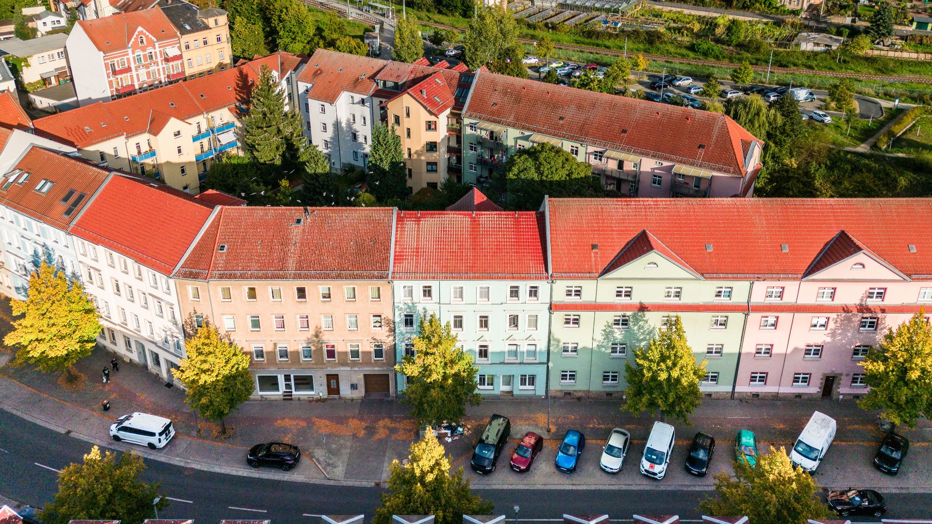Luftaufnahme von mehrstöckigen Wohnhäusern mit roten Dächern und parkenden Autos davor.