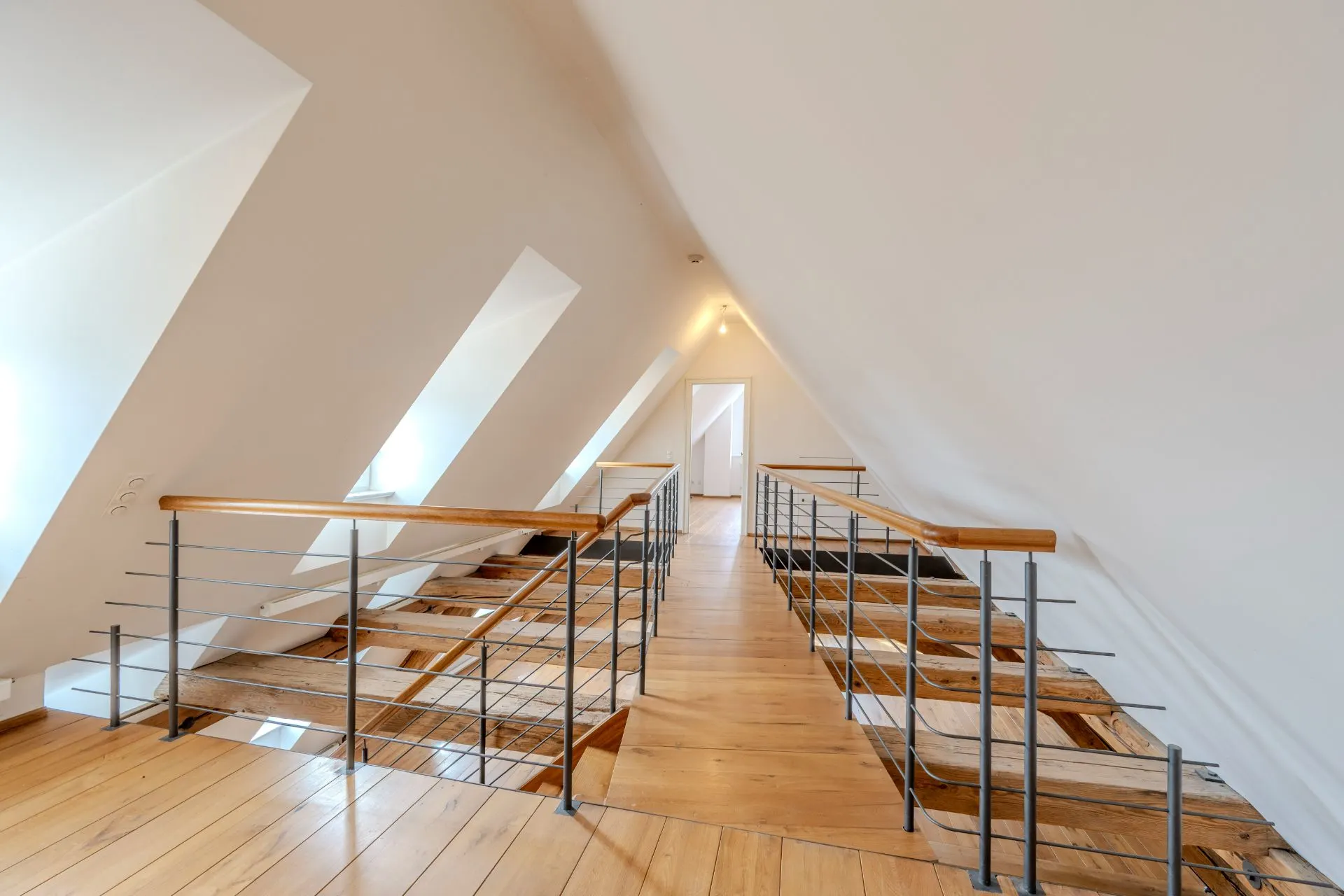 Dachgeschoss mit Holzfußboden, Geländer und schrägen Wänden mit Fenstern.