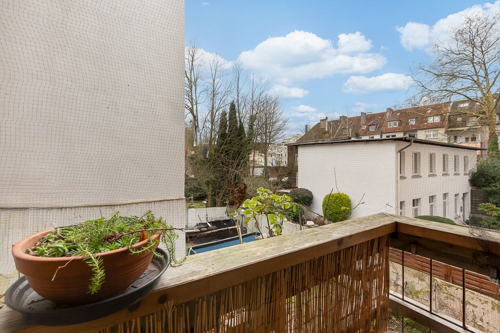 Balkon mit Pflanztopf, Blick auf Hof, Bäume und benachbarte Gebäude bei Tageslicht.