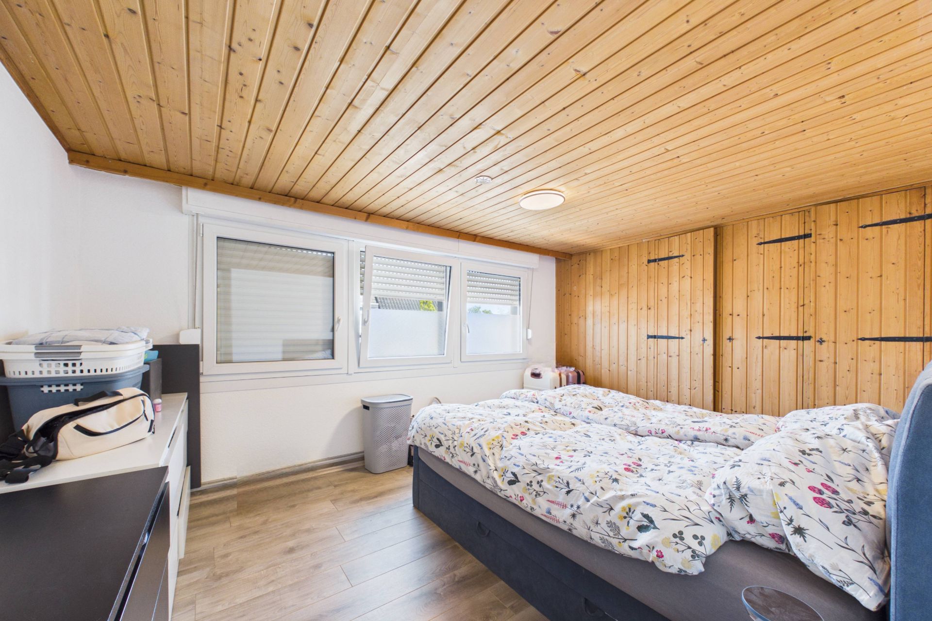 Helles Schlafzimmer mit Doppelbett, Holzdecke, großen Fenstern und Wandschränken aus Holz.