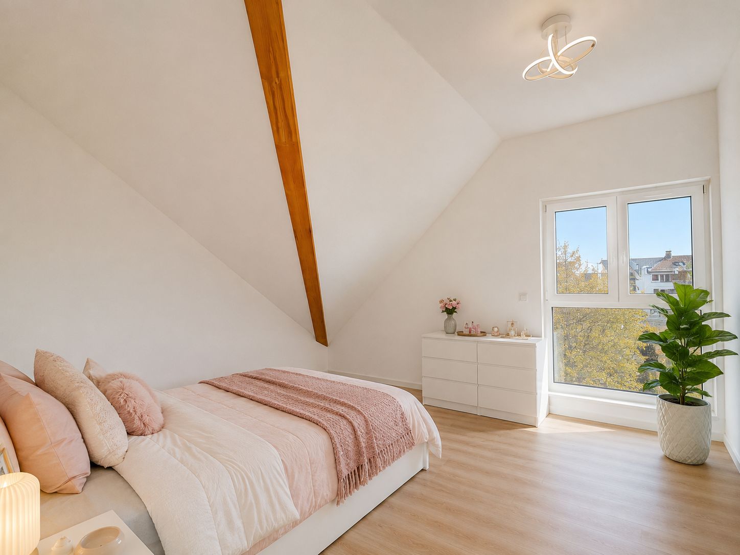 Helles Schlafzimmer mit schräger Decke, Doppelbett, Kommode und großem Fenster.