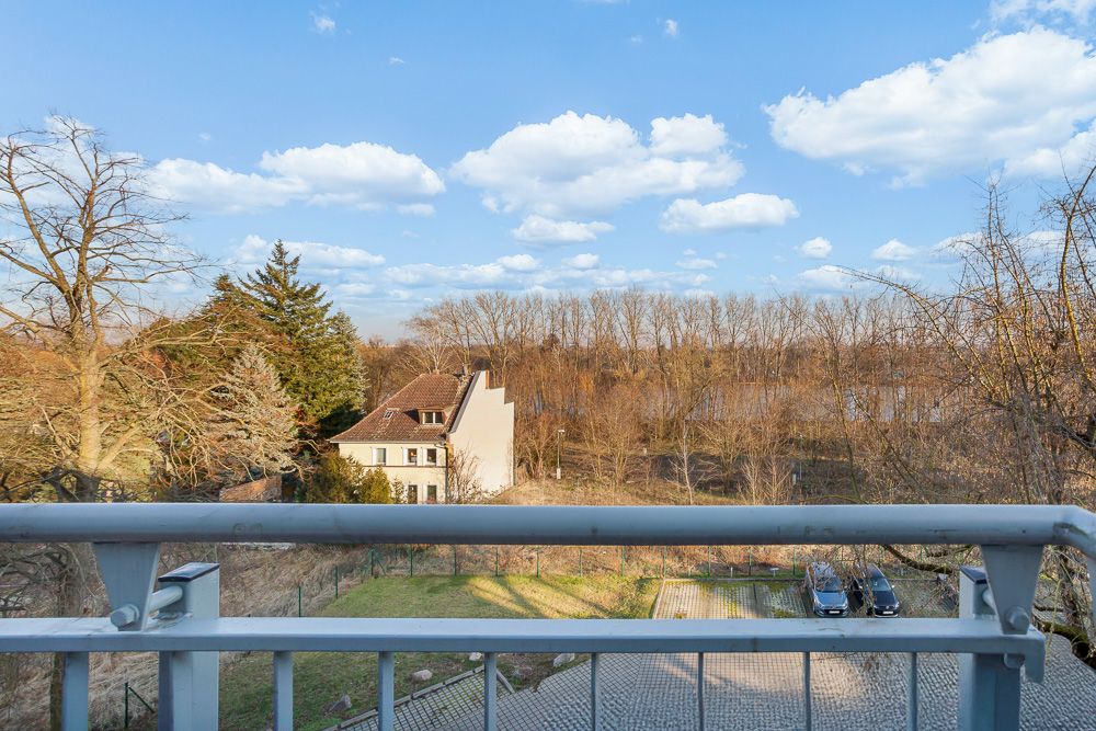 Blick von einem Balkon auf einen Garten, ein Wohnhaus und Bäume im Hintergrund.