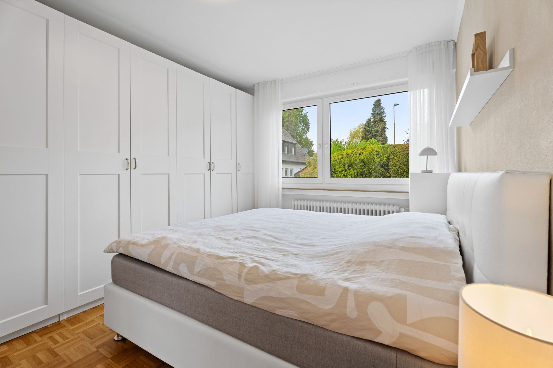 Helles Schlafzimmer mit großem Bett, weißem Kleiderschrank und Fenster mit Blick ins Grüne.