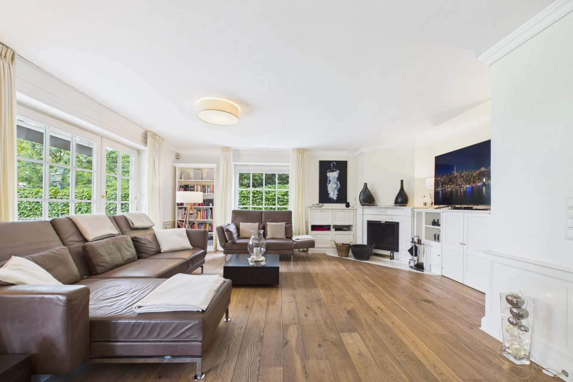 Helles Wohnzimmer mit braunen Sofas, Kamin, Bücherregal und großem Fenster.