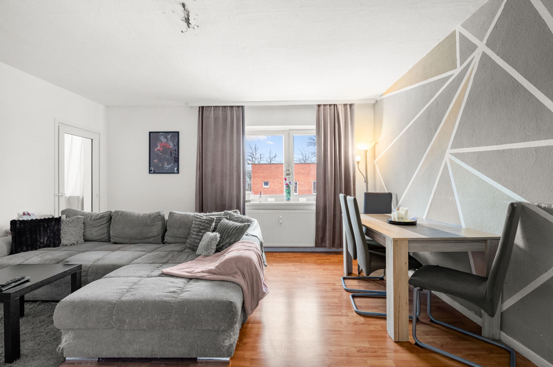 Wohnzimmer mit grauem Ecksofa, Esstisch, Stühlen und geometrisch gemusterter Wand.