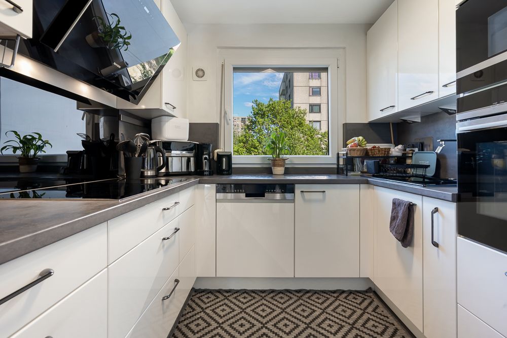 Moderne Küche mit weißen Schränken, Küchengeräten und einem Fenster mit Blick auf Bäume.
