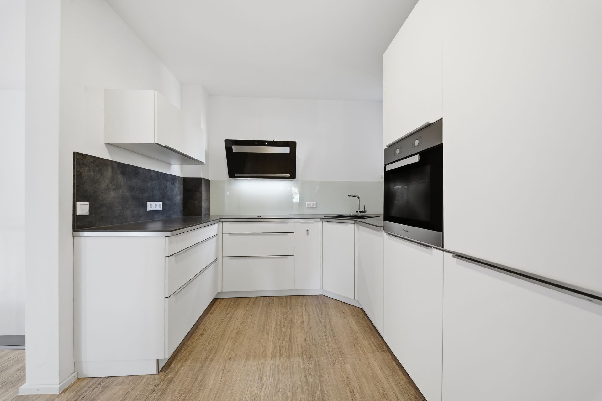 Moderne weiße Einbauküche mit Backofen, Kochfeld und Holzfußboden.