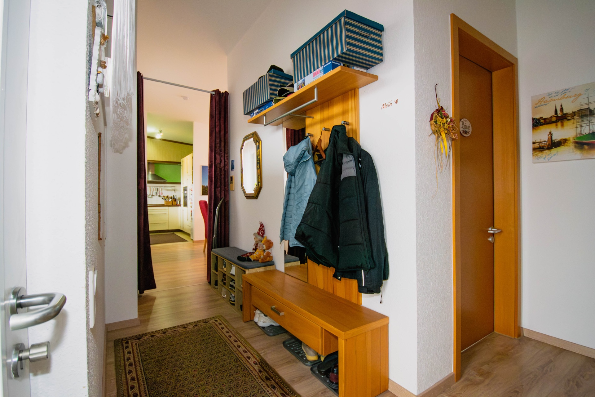 Flur mit Garderobe, Schuhbank, Spiegel und Blick in eine Küche.