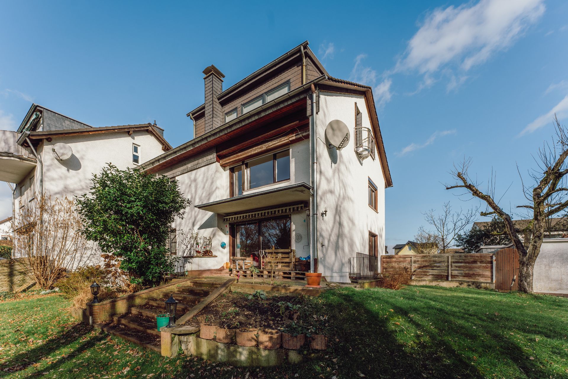Zweistöckiges Wohnhaus mit Balkon, Garten und Terrasse bei sonnigem Wetter.