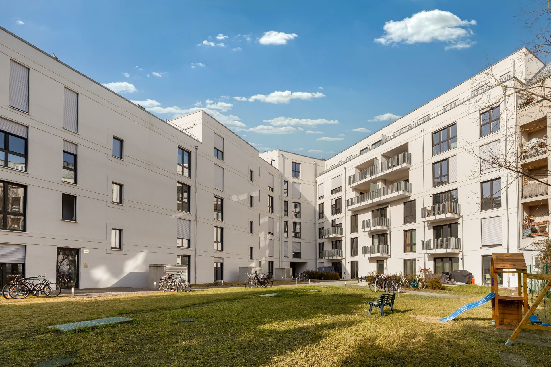 Moderner Innenhof mit Rasenfläche, Spielplatz, Fahrrädern und Wohngebäuden im Hintergrund.