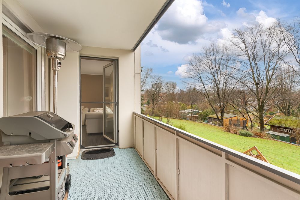 Balkon mit Grill, Heizstrahler und Blick auf einen Garten mit Bäumen.