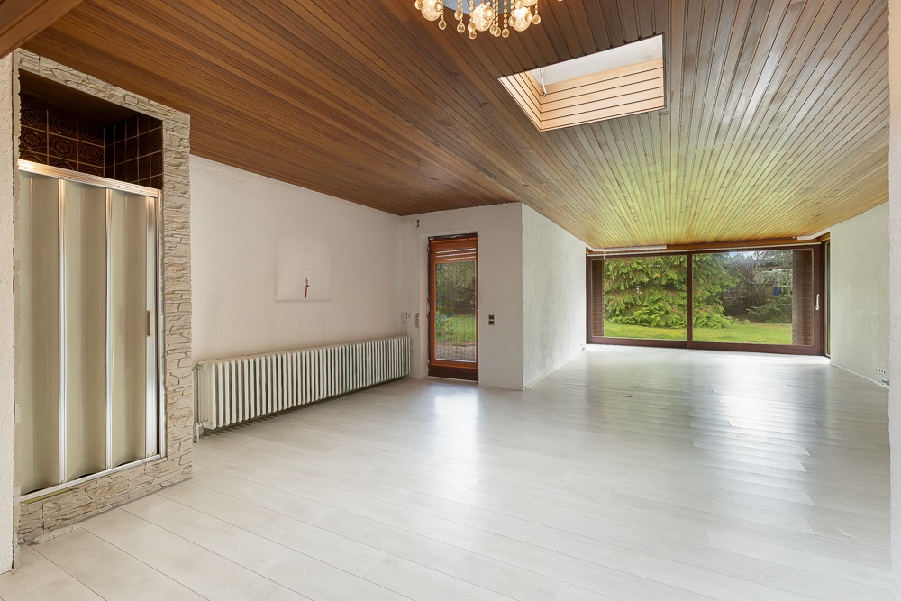 Heller Wohnraum mit Holzbalkendecke, großen Fenstern, Dusche und Blick in den Garten.