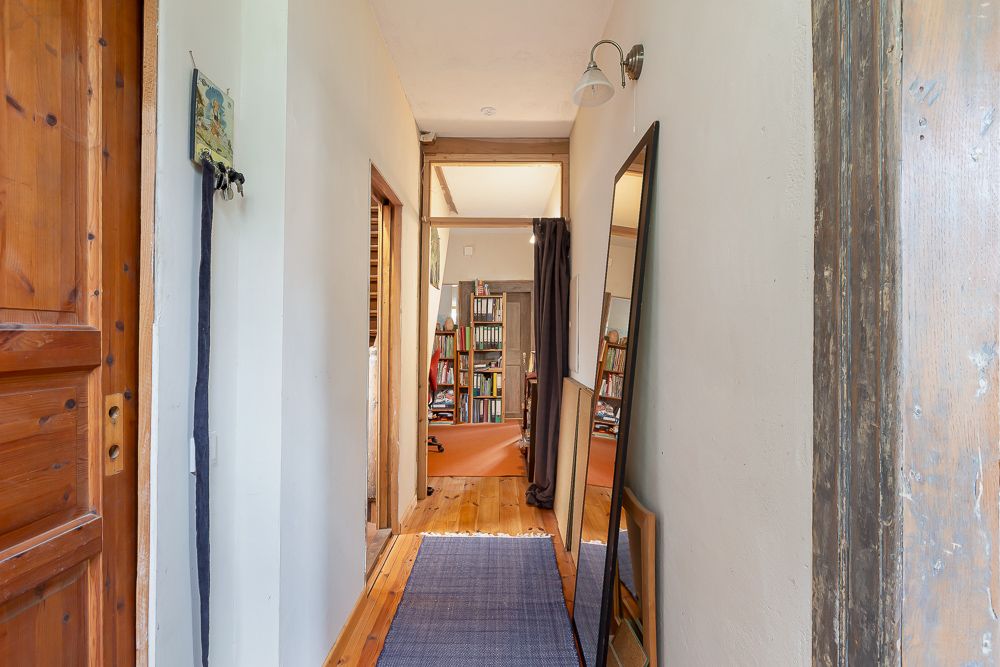 Heller Flur mit Spiegel, Holztür und Blick auf ein Zimmer mit Bücherregalen.
