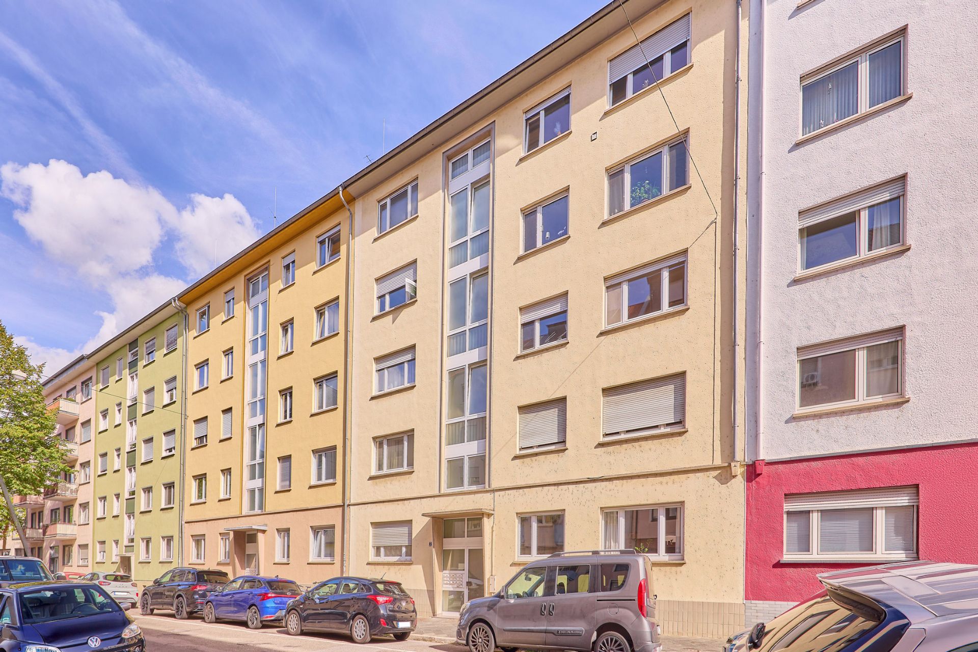 Mehrstöckiges Wohnhaus mit parkenden Autos davor an einer ruhigen Straße.