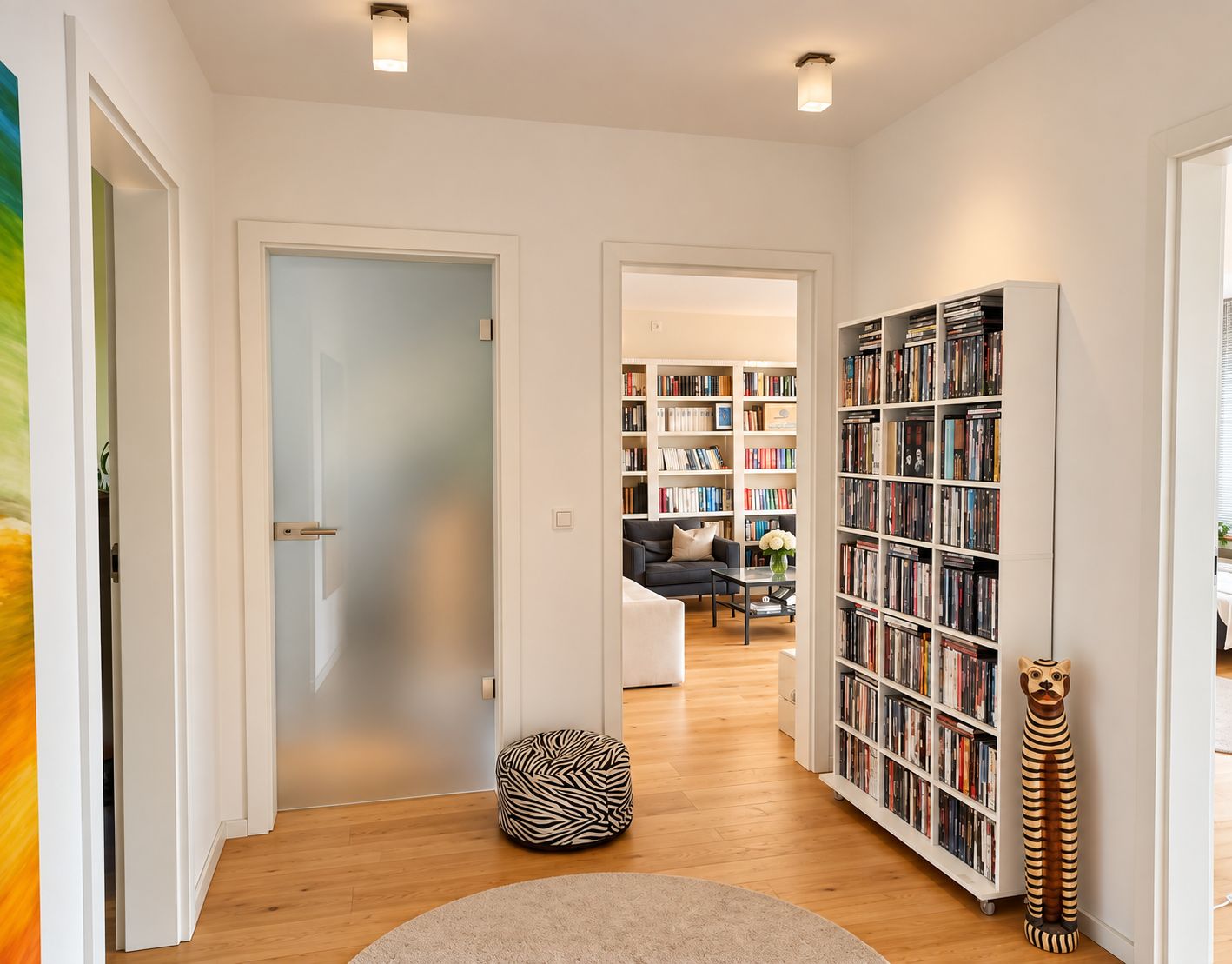 Heller Flur mit Bücherregal, rundem Teppich und Zebra-Hocker, Zugang zu Wohnzimmer.