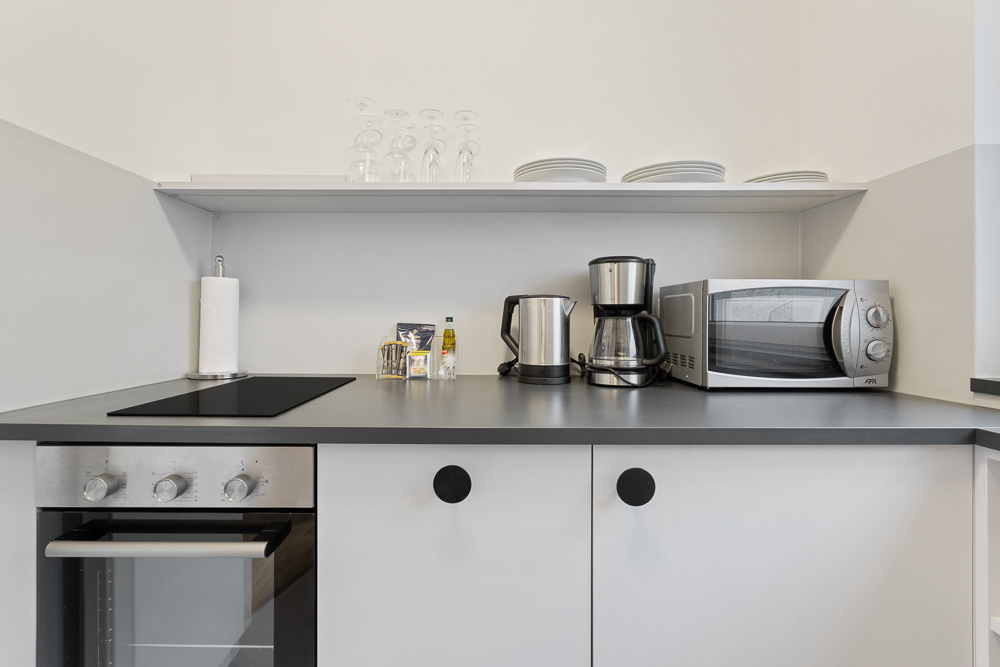 Moderne Küche mit Herd, Ofen, Wasserkocher, Kaffeemaschine, Mikrowelle und Regal mit Geschirr.