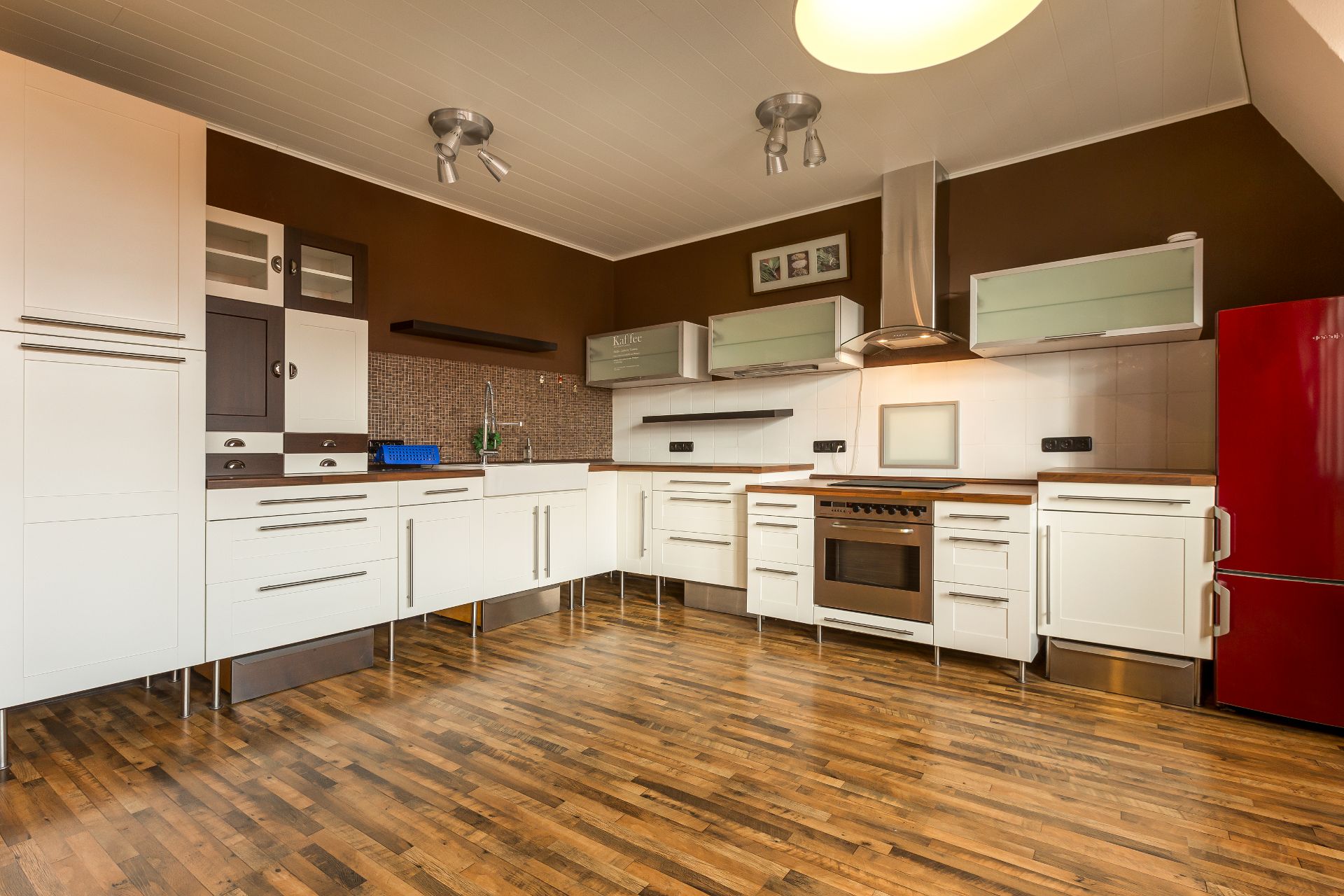 Moderne Küche mit weißen Schränken, brauner Wand, Holzfußboden und rotem Kühlschrank.