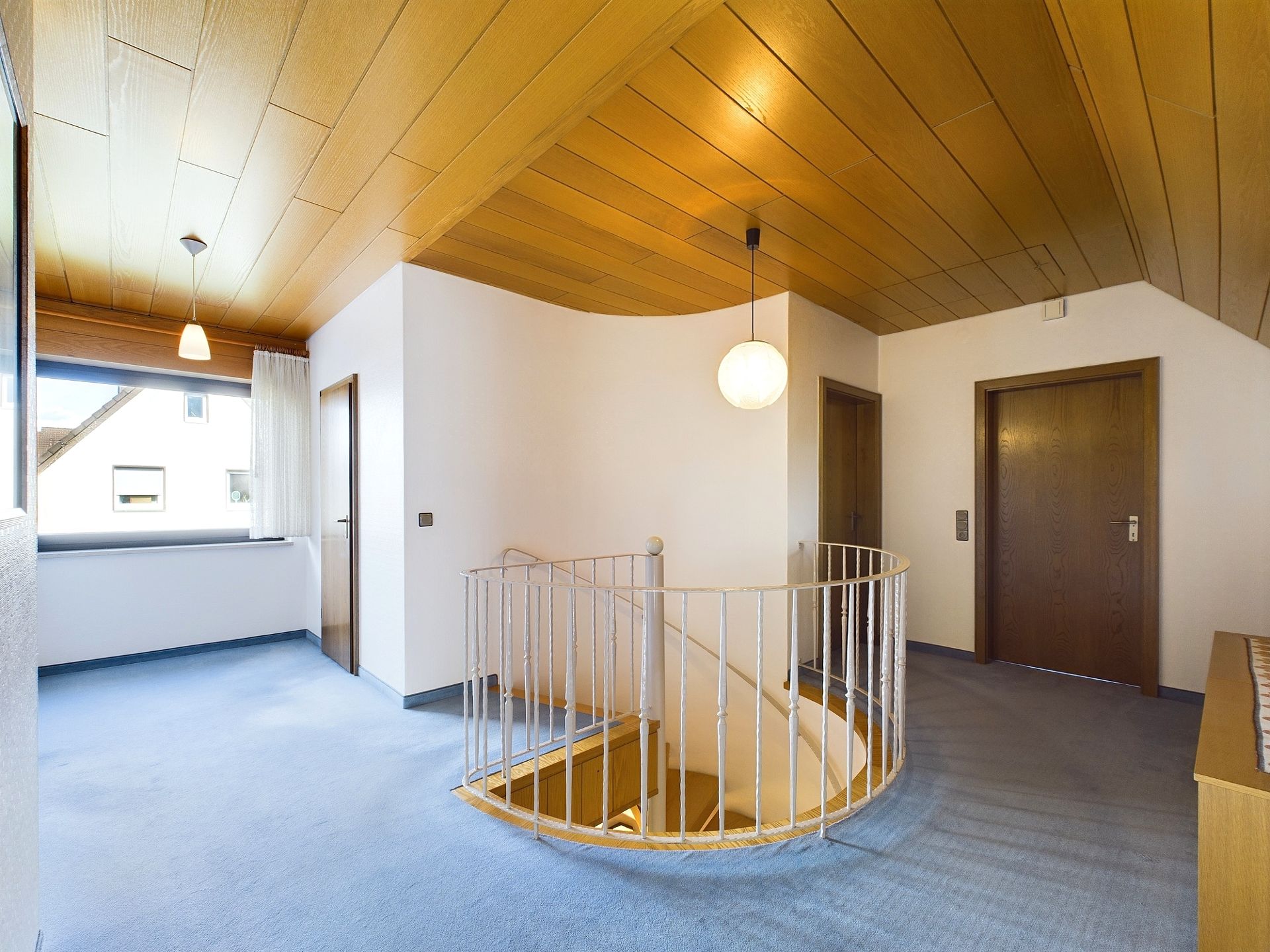 Heller Flur mit Holzdecke, Teppichboden und runder Treppe in einer Wohnimmobilie.