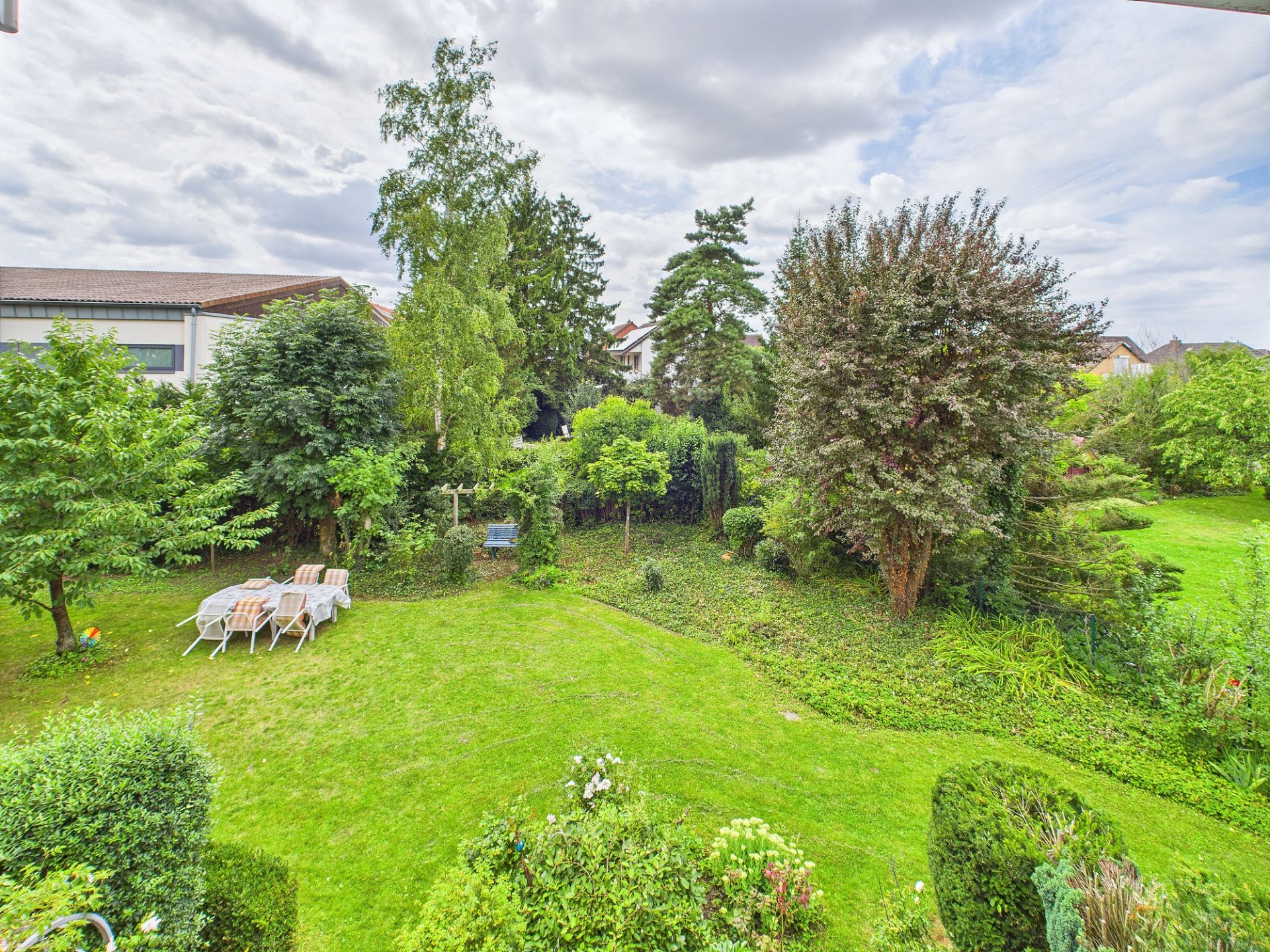 Großer Garten mit Rasen, Bäumen und Gartenmöbeln auf der linken Seite.