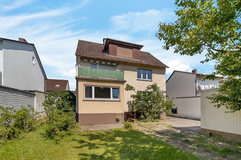 Zweistöckiges Wohnhaus mit Balkon, Garten und Einfahrt, umgeben von Bäumen und Nachbarhäusern.