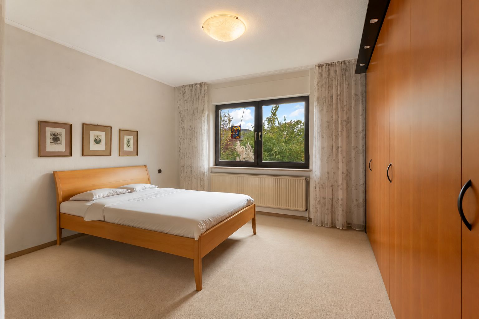 Schlafzimmer mit Holzbett, großem Kleiderschrank und Fenster mit Blick ins Grüne.