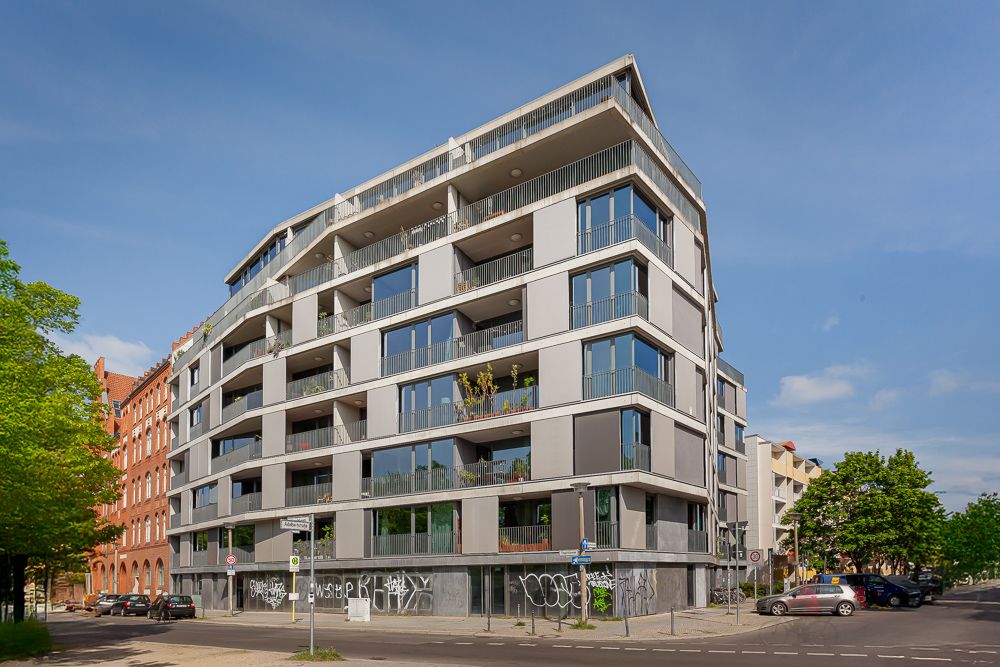Modernes Wohngebäude mit mehreren Balkonen an einer Straßenecke, Graffiti am Erdgeschoss.