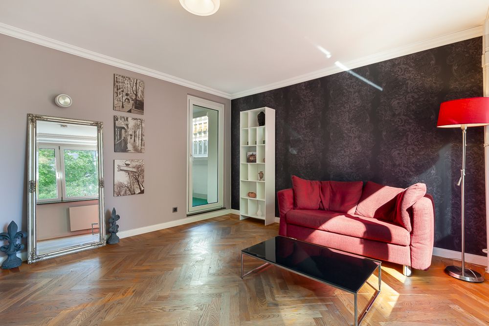 Wohnzimmer mit rotem Sofa, schwarzem Couchtisch, Regal und Stehlampe auf Parkettboden.