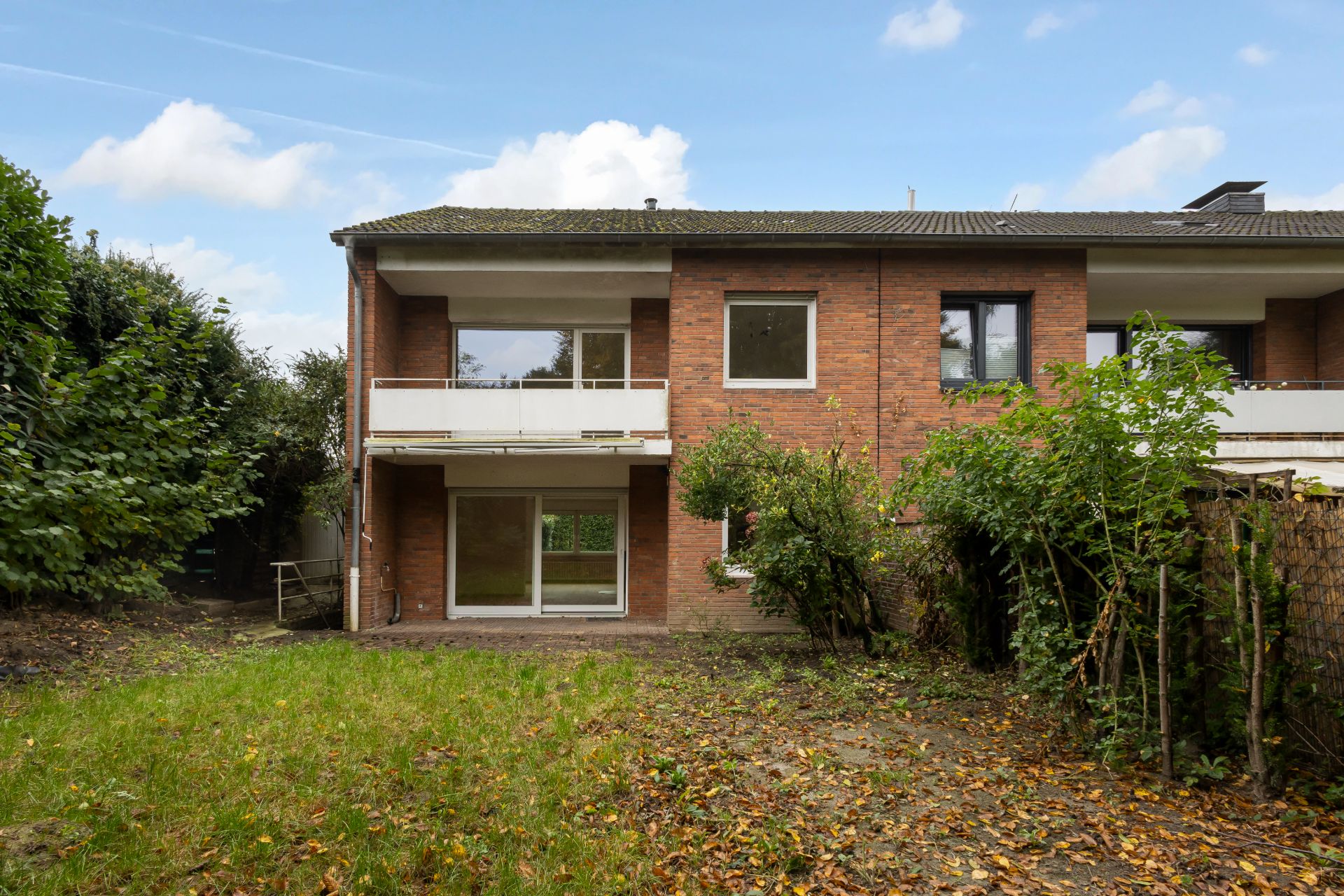 Rückseite eines zweistöckigen Hauses mit Balkon, Garten und großen Fenstern.