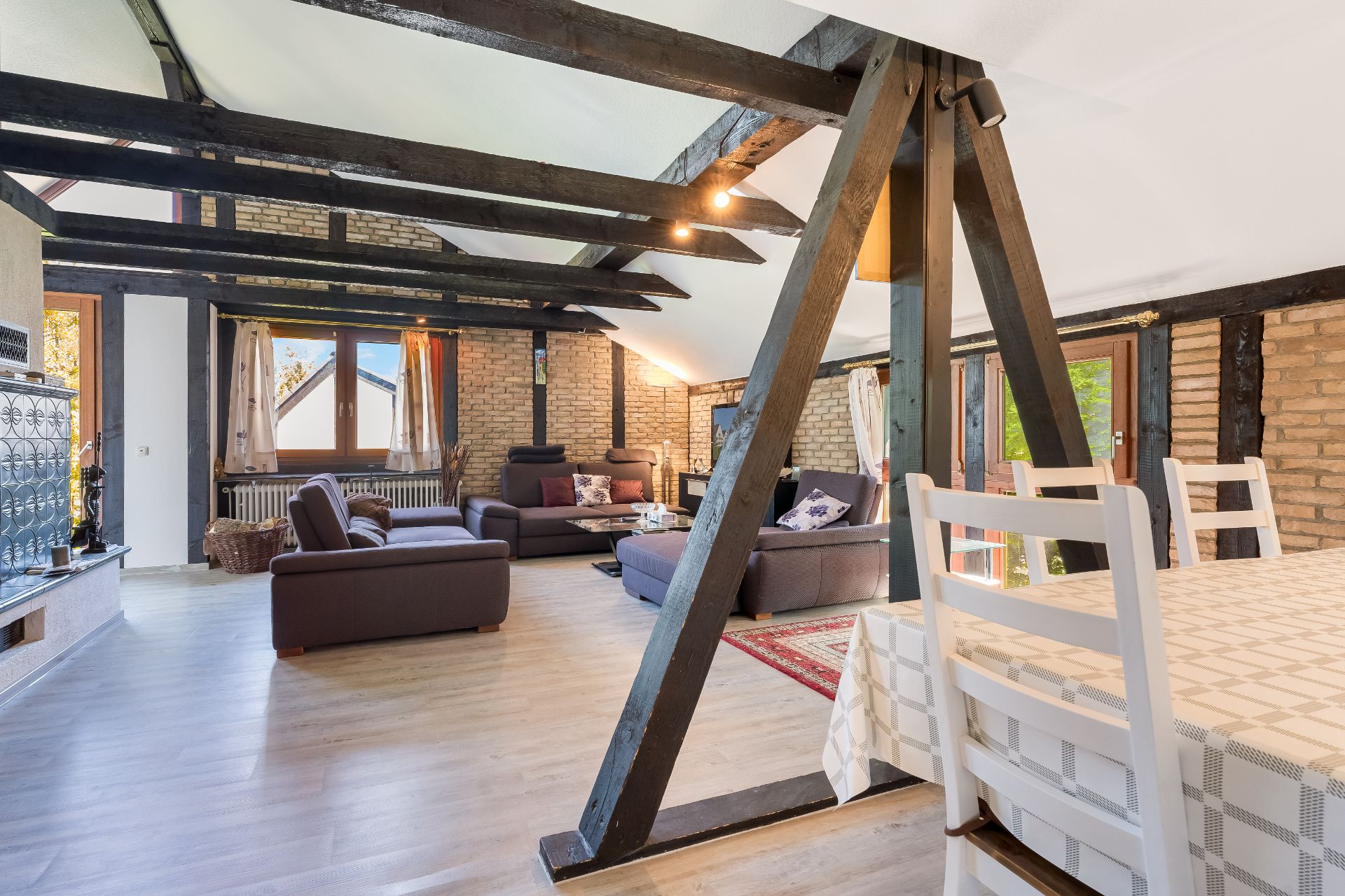 Helles Wohnzimmer mit Holzbalken, Sofas, Esstisch und großen Fenstern.