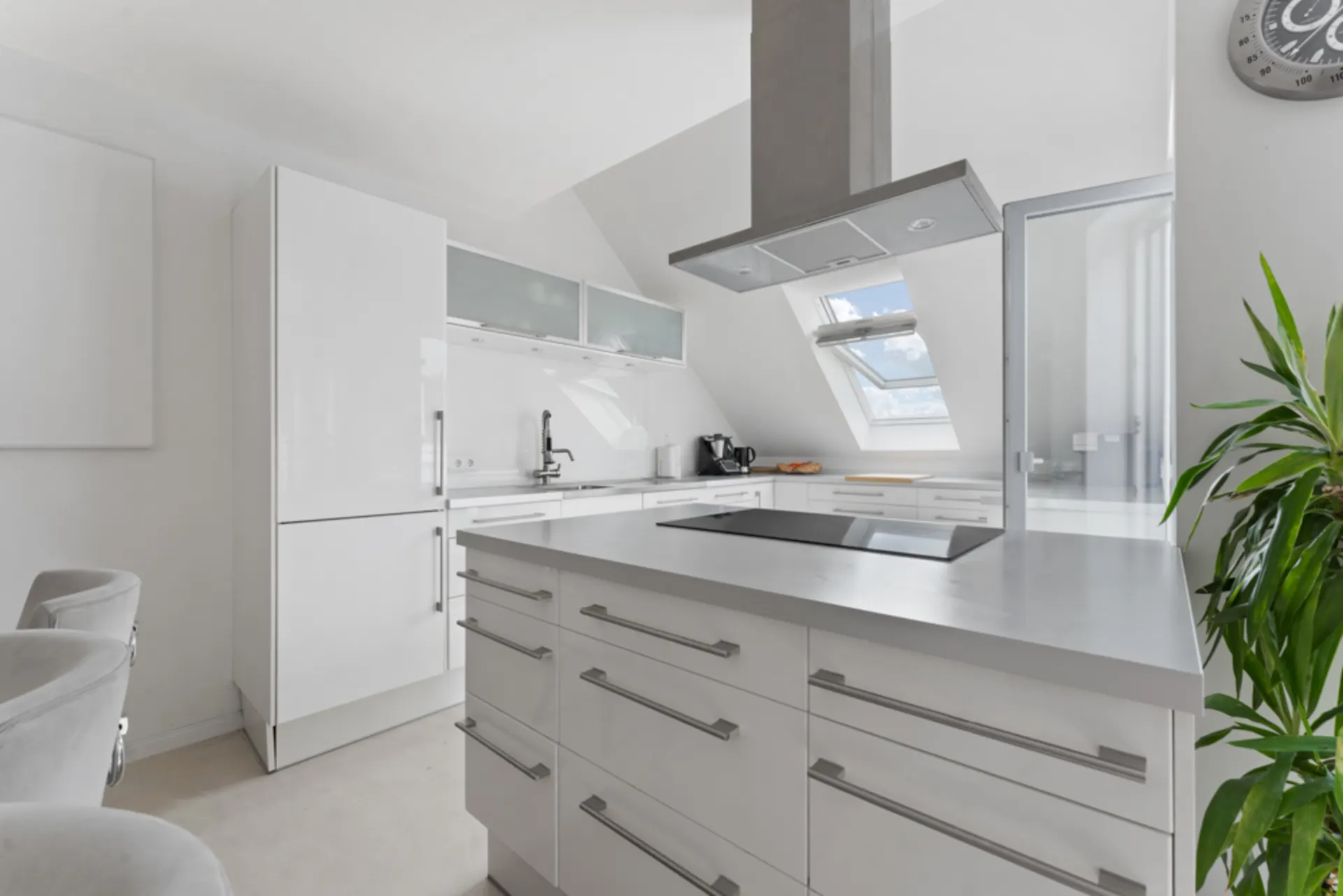 Moderne weiße Küche mit Kochinsel, Dachfenster und Pflanzen im Raum.