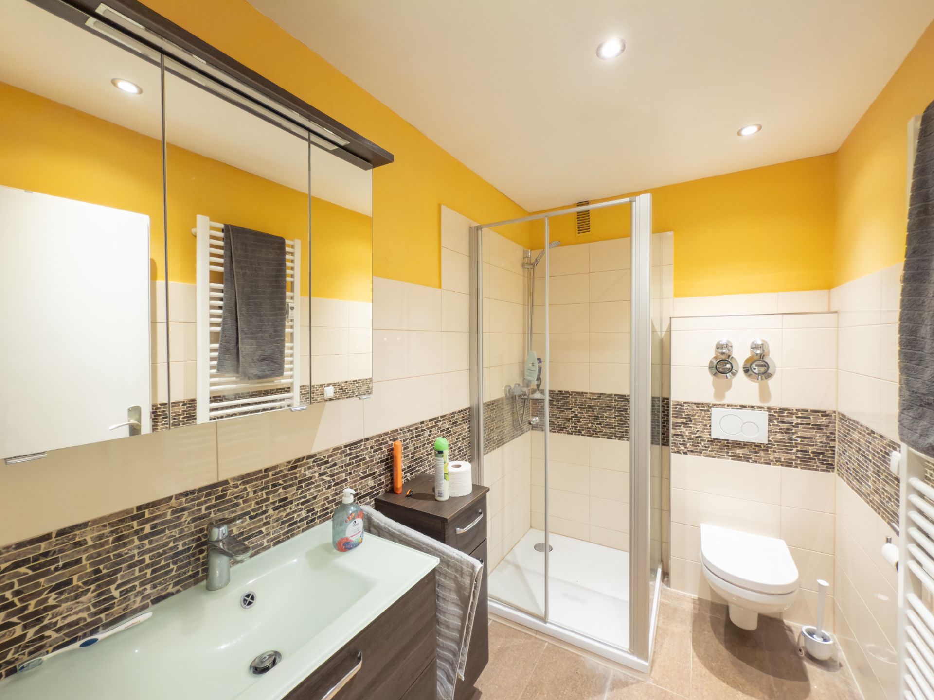 Modernes Badezimmer mit Dusche, Waschbecken, Wandspiegel und gelben Wänden.