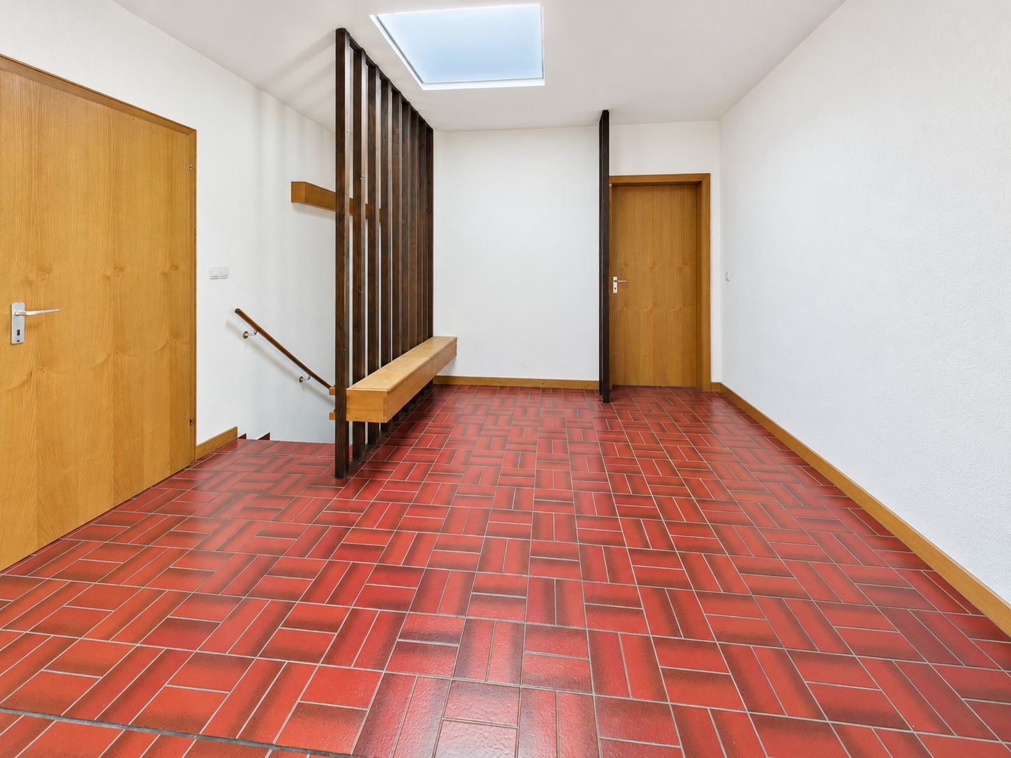Flur mit roten Bodenfliesen, Holztüren, Wandgarderobe und Oberlicht.