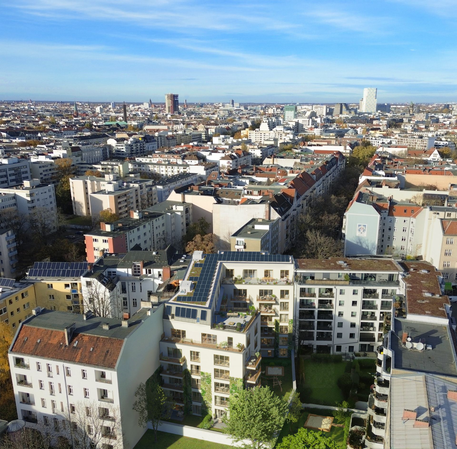 Blick auf mehrere Wohnhäuser mit Balkonen und begrünten Innenhöfen in einer Stadt.