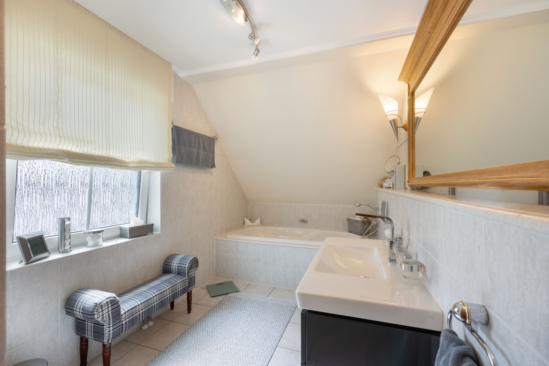 Helles Badezimmer mit Badewanne, großem Spiegel, Fensterbank und Sitzbank.
