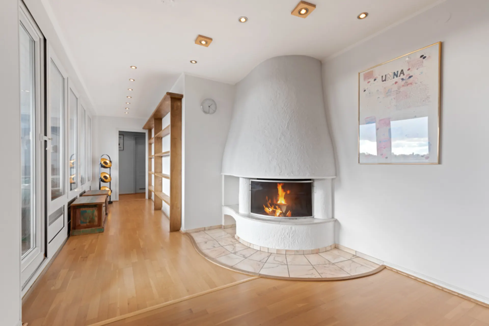 Heller Raum mit Holzfußboden, Kamin, Regal und großen Fenstern.