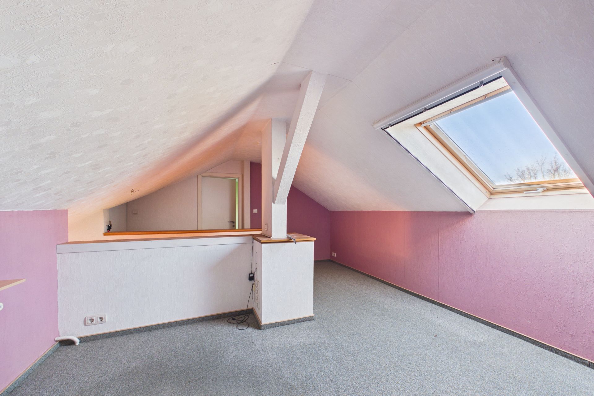 Dachzimmer mit schräger Decke, lila Wänden, Dachfenster und Teppichboden.