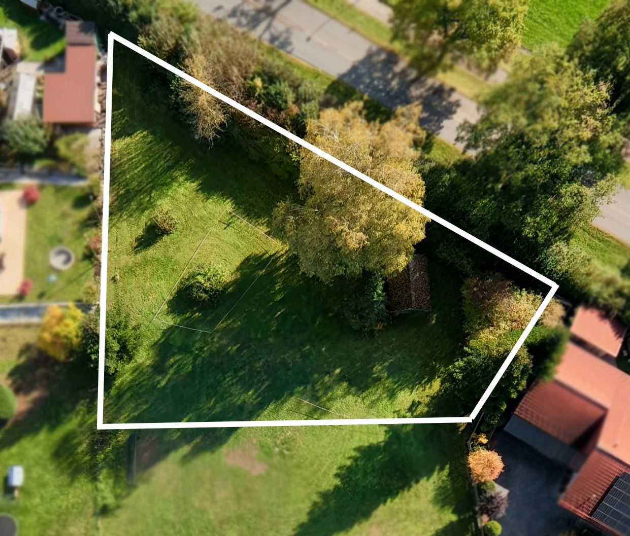 Luftaufnahme eines dreieckigen, von Bäumen umgebenen Gartengrundstücks mit Rasen.