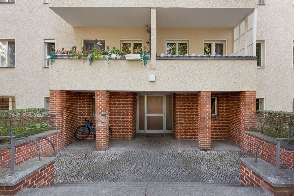 Eingangsbereich eines Wohnhauses mit Fahrrad und Balkon mit Pflanzen darüber.