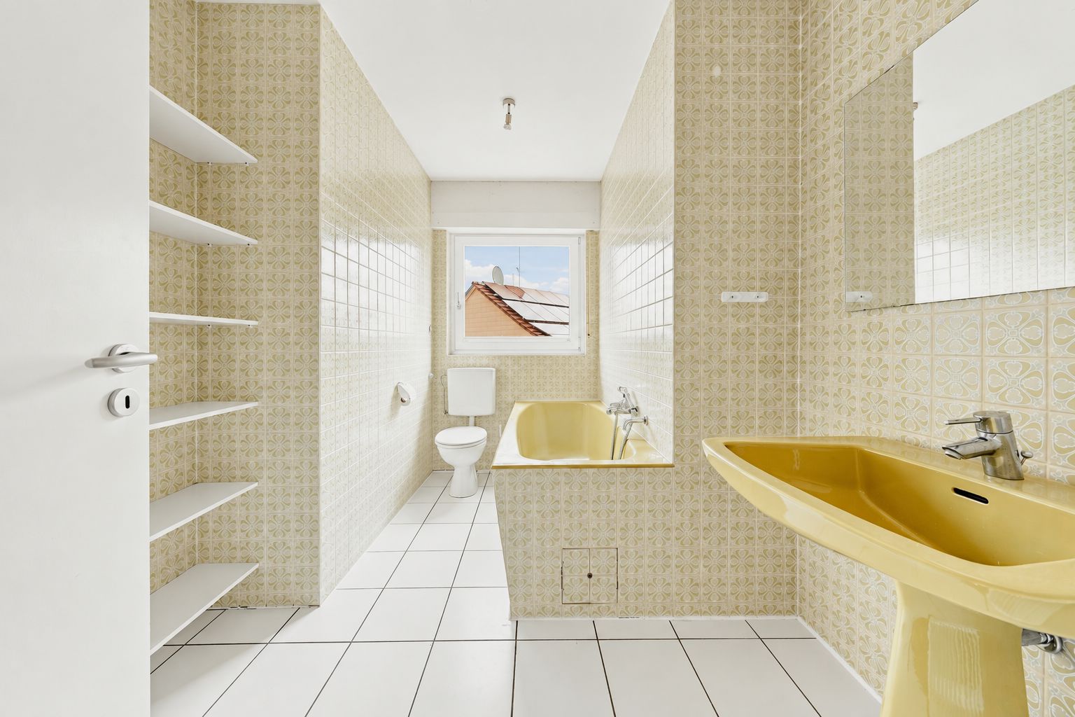Helles Badezimmer mit gelber Badewanne, gelbem Waschbecken, Regal, Toilette und Fenster.