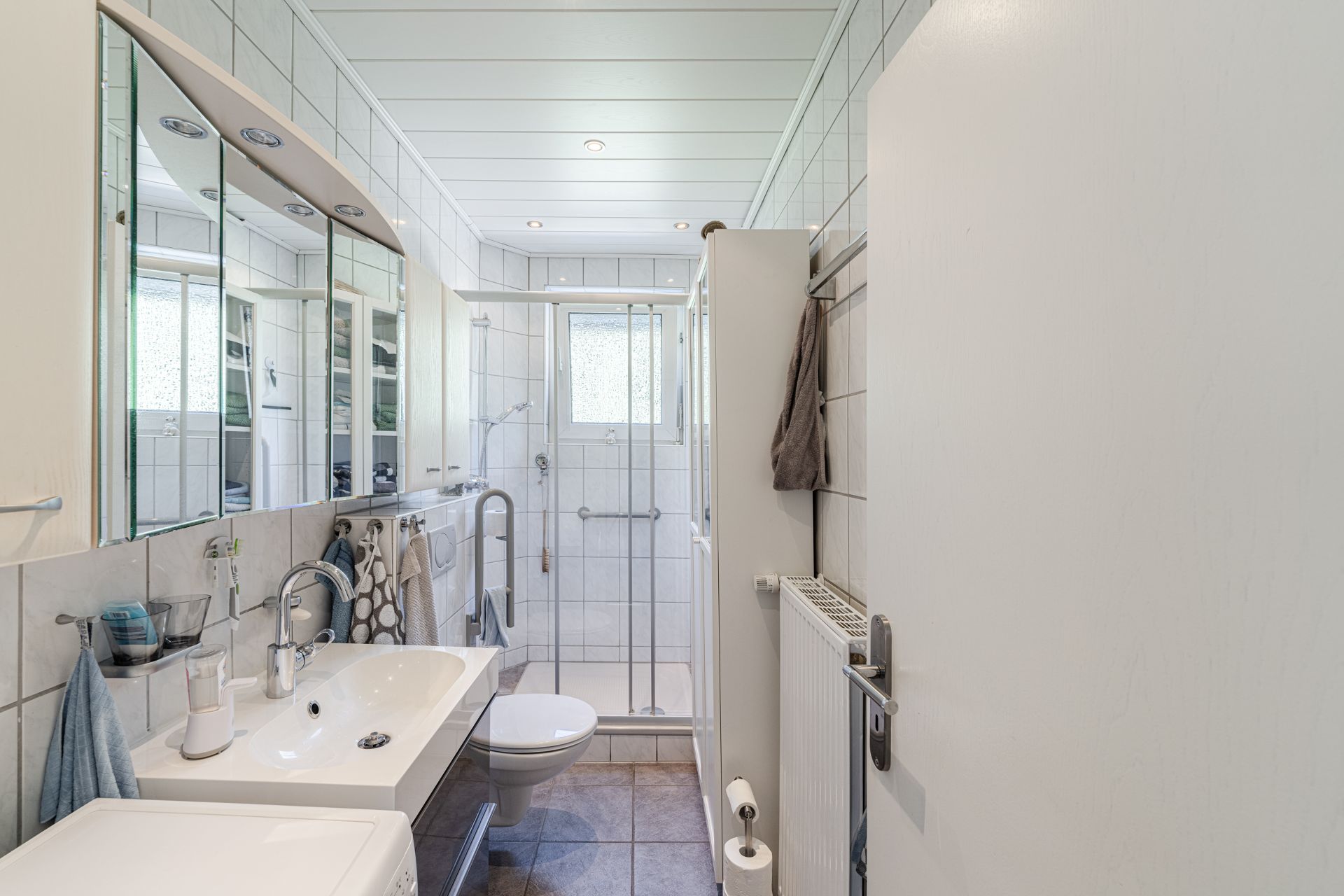 Modernes Badezimmer mit Dusche, Waschbecken, Spiegel, Toilette und Handtüchern.