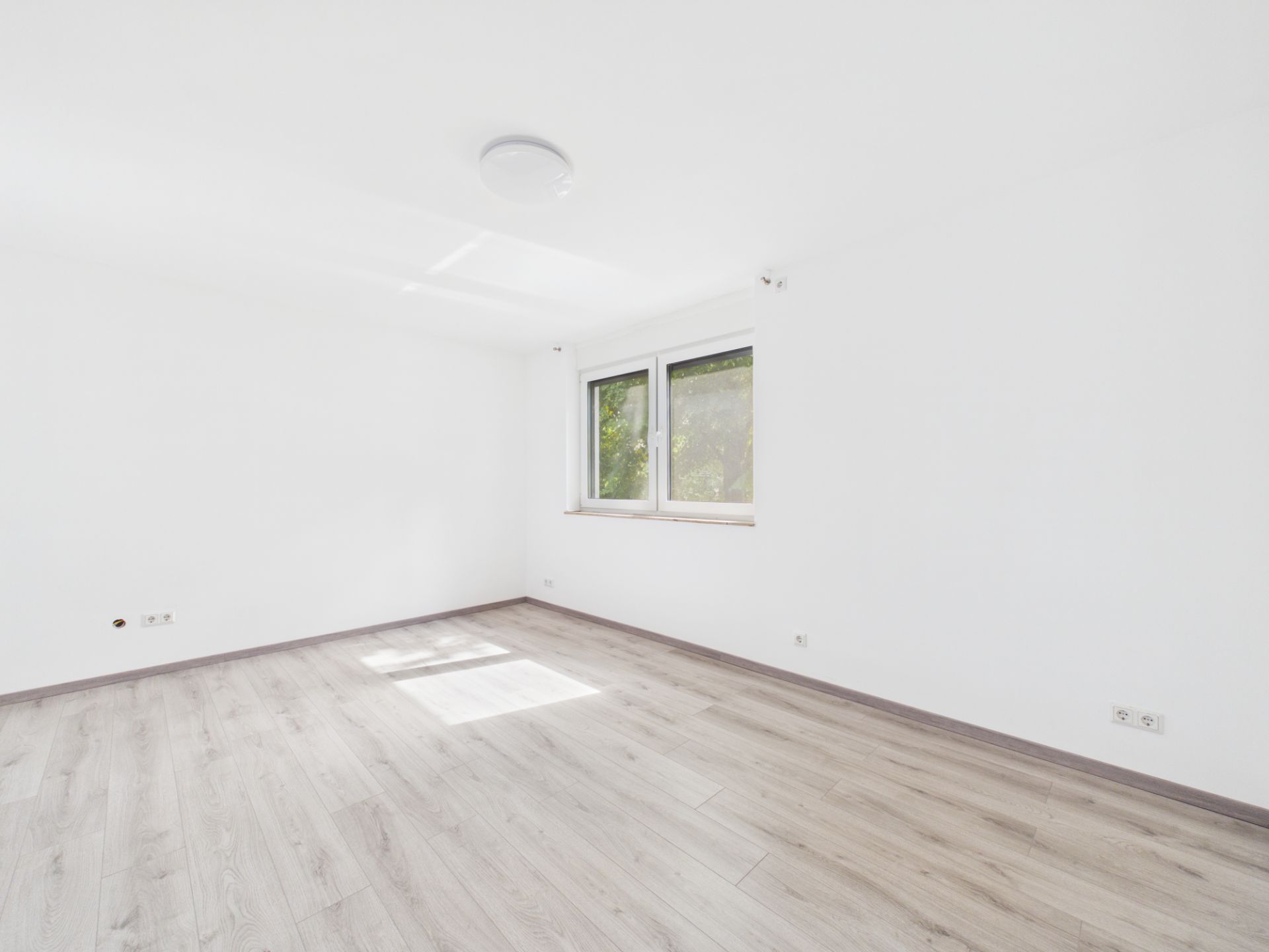 Leerer, heller Raum mit weißem Wänden, Holzfußboden und einem Fenster.
