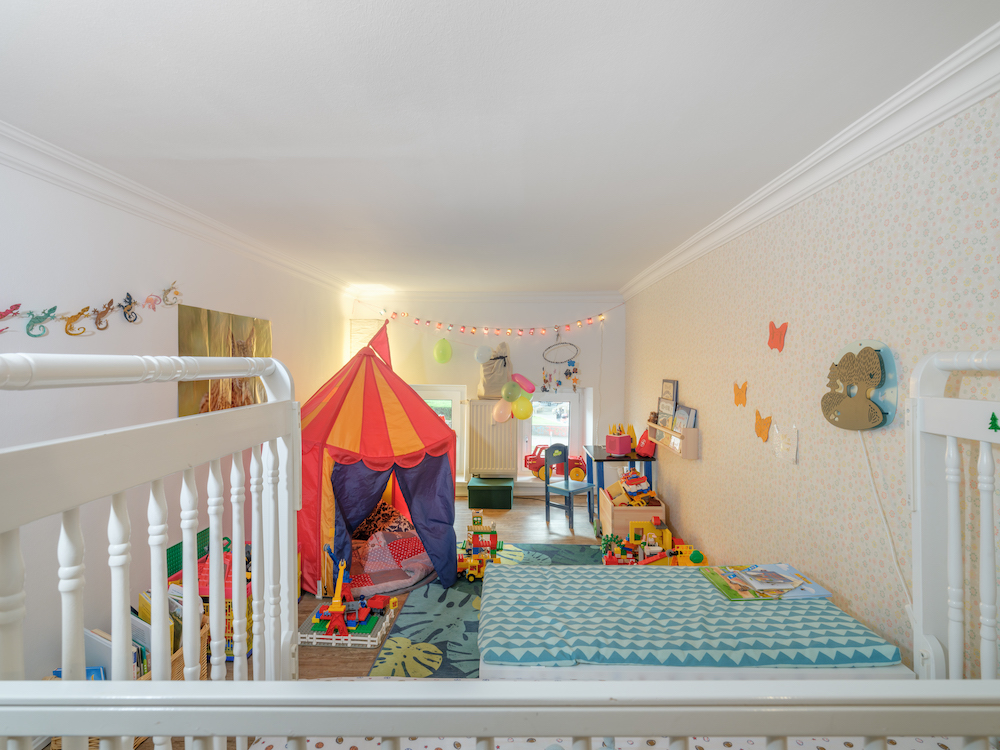 Helles Kinderzimmer mit Spielzelt, Spielzeugen, zwei Betten und bunter Dekoration.