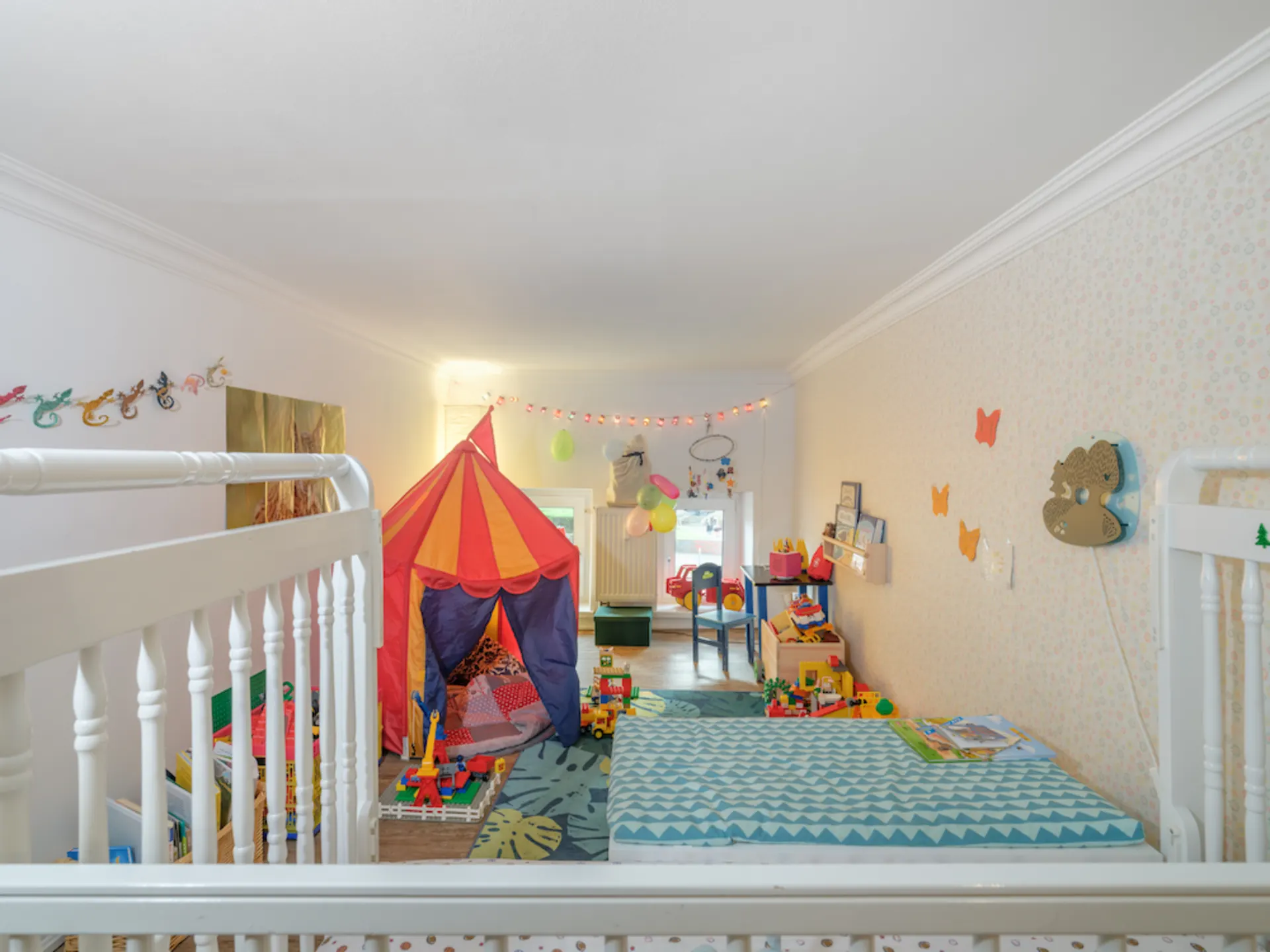 Helles Kinderzimmer mit Spielzelt, Spielzeugen, zwei Betten und bunter Dekoration.