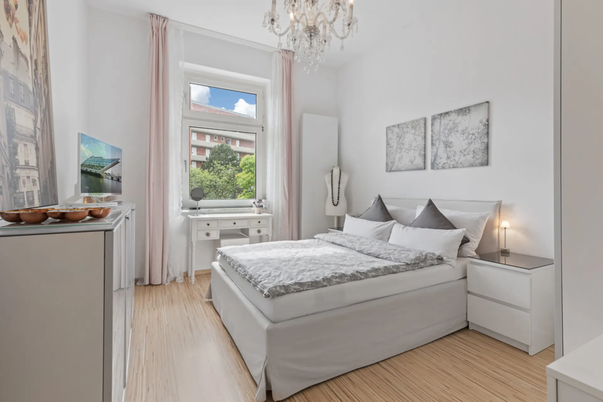Helles Schlafzimmer mit Doppelbett, Schreibtisch am Fenster und Kronleuchter.