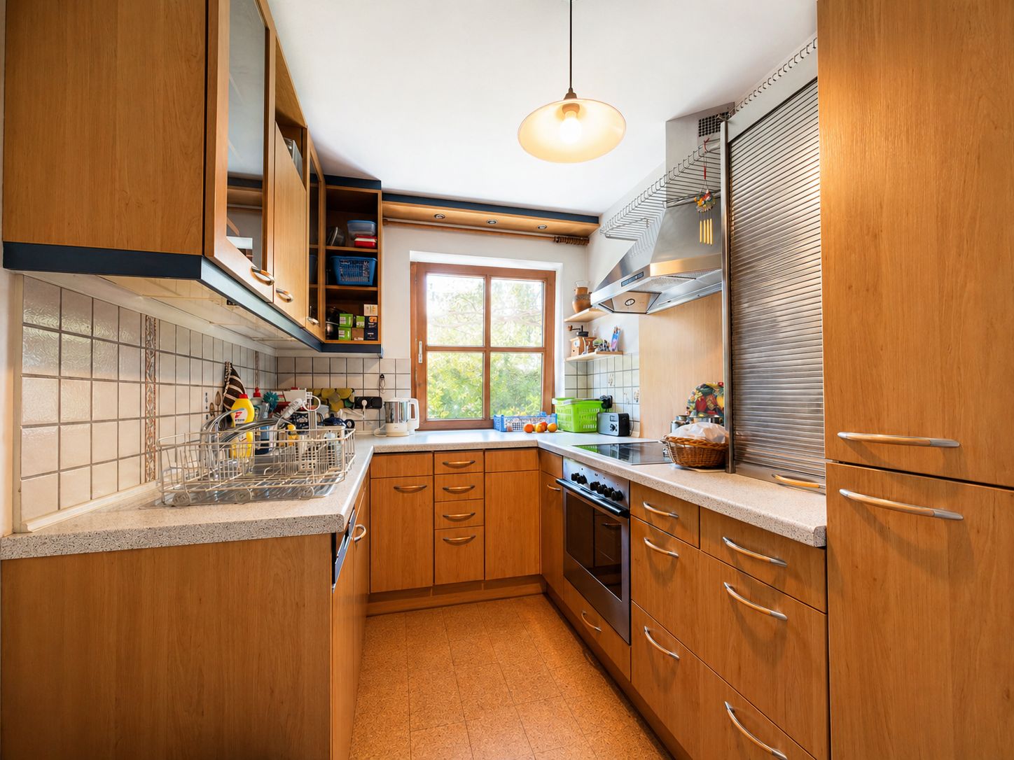 Helle Küche mit Holzschränken, Herd, Spüle und Fenster mit Blick ins Grüne.