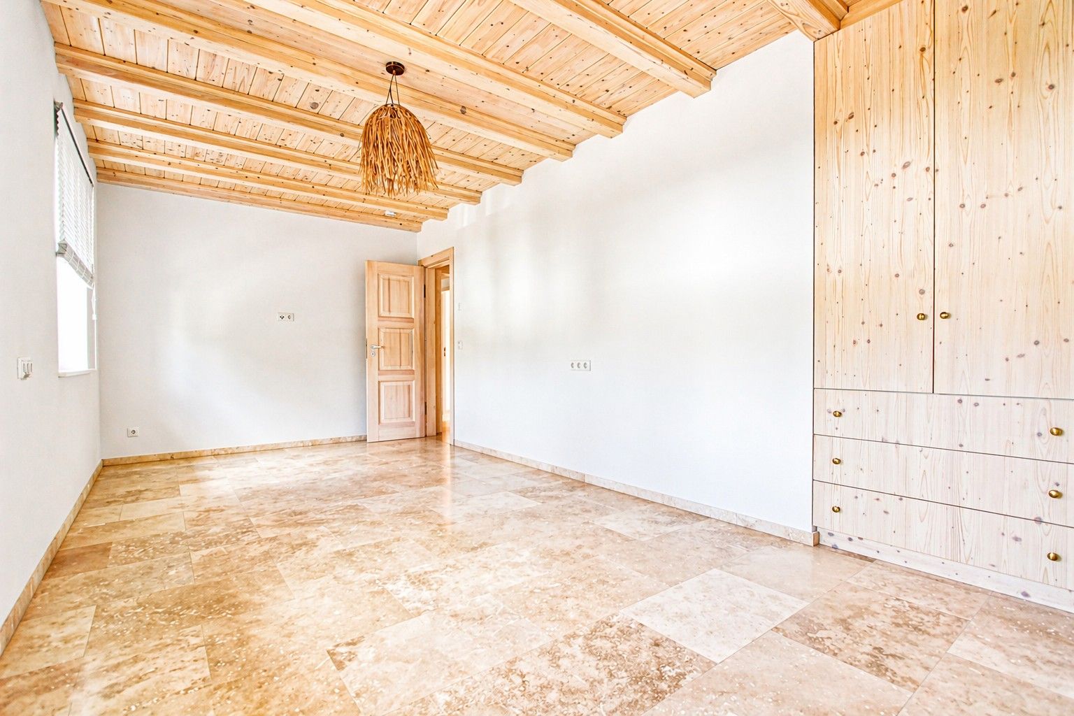 Heller Raum mit Holzbalkendecke, Einbauschrank und Fliesenboden.